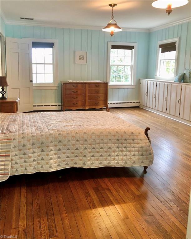 unfurnished bedroom featuring hardwood / wood-style flooring, baseboard heating, and crown molding