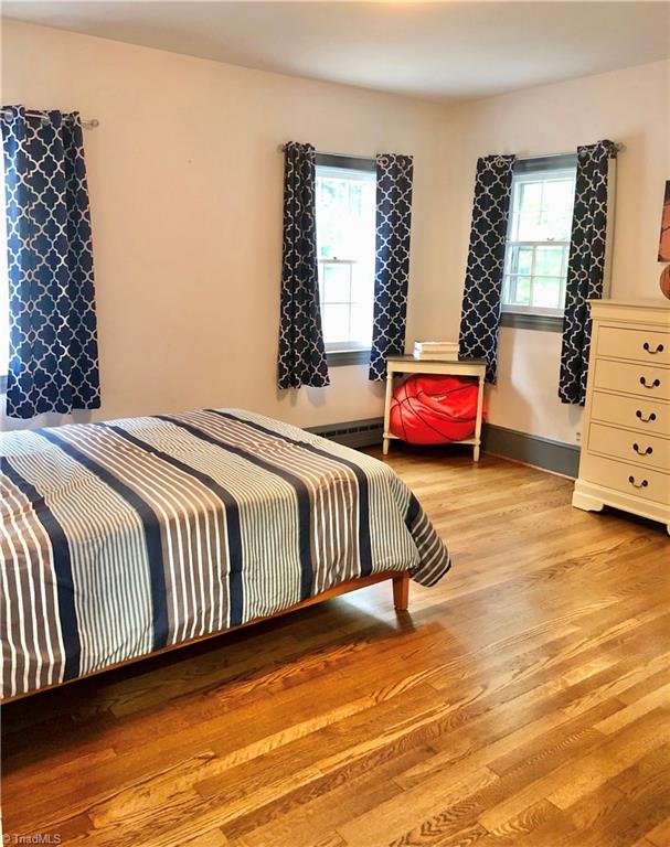 bedroom featuring baseboard heating, light hardwood / wood-style floors, and multiple windows