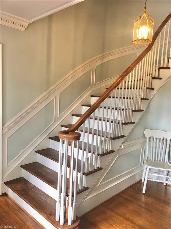 stairs featuring wood-type flooring, crown molding, and an inviting chandelier