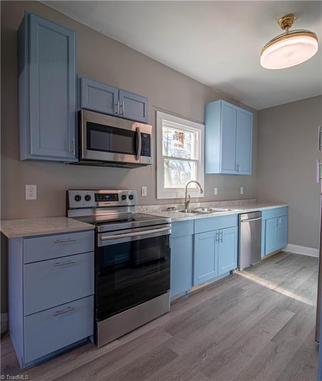 kitchen featuring sink, blue cabinetry, stainless steel appliances, and light wood-type flooring