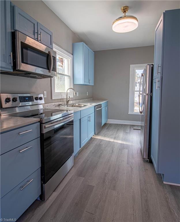 kitchen with appliances with stainless steel finishes, dark hardwood / wood-style flooring, plenty of natural light, blue cabinetry, and sink