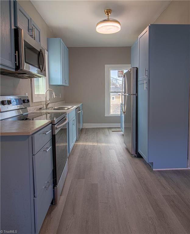 kitchen featuring appliances with stainless steel finishes, light hardwood / wood-style floors, blue cabinetry, and sink