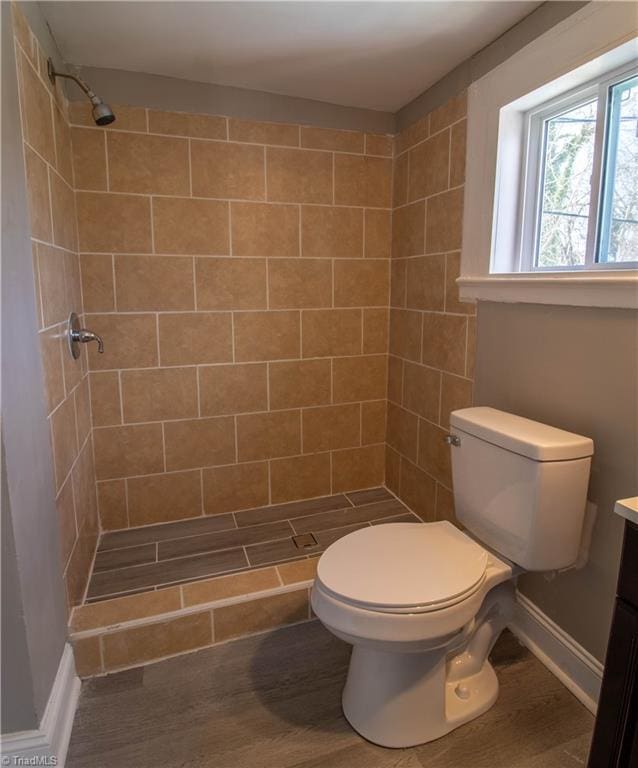 bathroom with hardwood / wood-style floors, tiled shower, vanity, and toilet