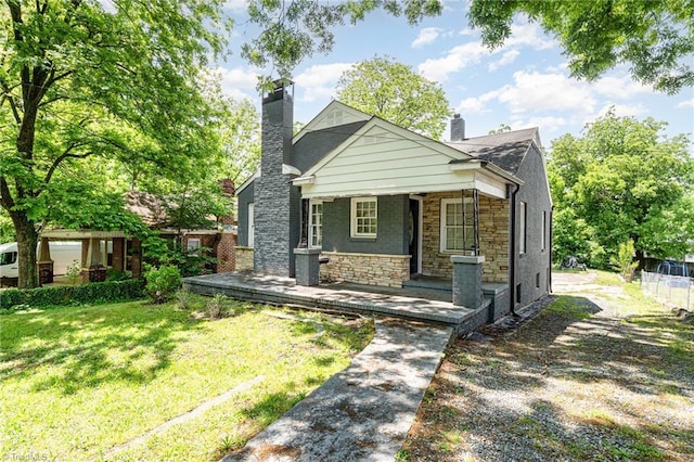 bungalow-style home featuring a chimney, a porch, stone siding, and a front yard