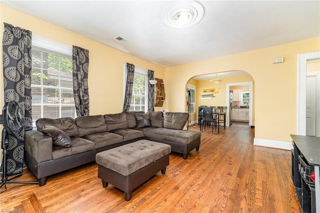 living room with arched walkways, light wood-style flooring, and baseboards