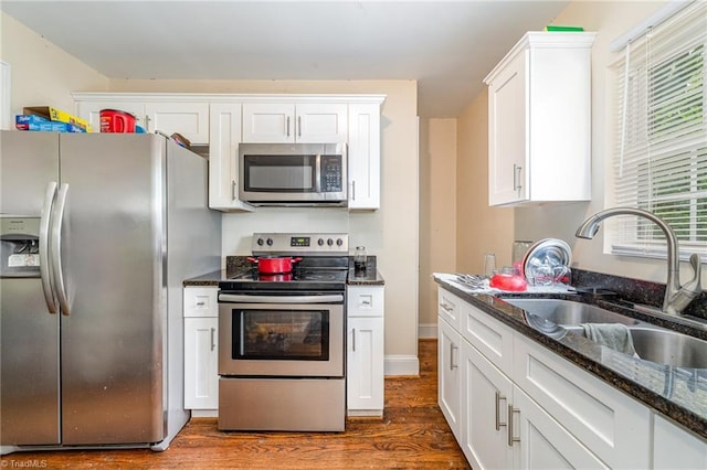 kitchen with stainless steel appliances, a sink, dark wood finished floors, white cabinets, and dark stone countertops