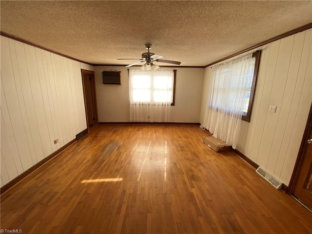 spare room featuring a textured ceiling, hardwood / wood-style flooring, an AC wall unit, and ceiling fan