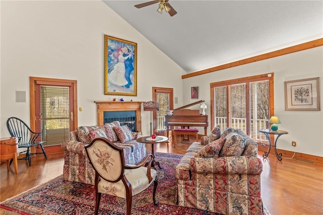 living area featuring baseboards, a ceiling fan, wood finished floors, a fireplace, and high vaulted ceiling