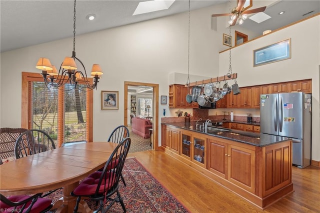 dining area featuring light wood-style floors, plenty of natural light, a skylight, and ceiling fan with notable chandelier