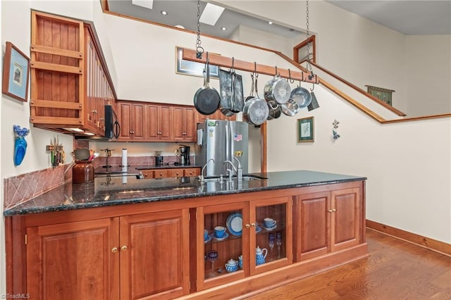 kitchen featuring black microwave, a sink, freestanding refrigerator, brown cabinetry, and dark stone countertops