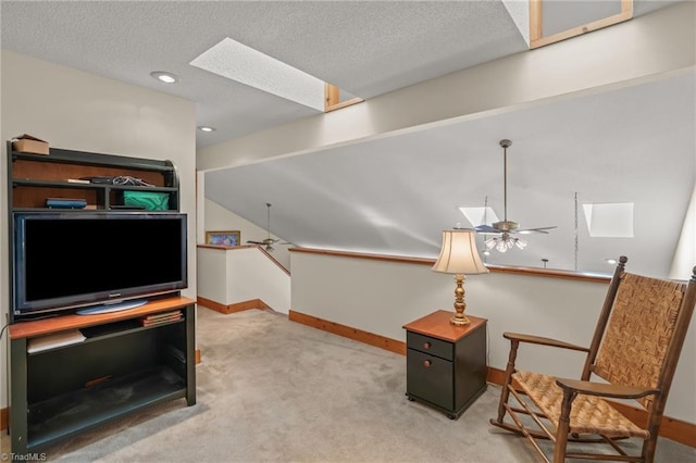 sitting room featuring a textured ceiling, light colored carpet, an upstairs landing, baseboards, and a ceiling fan