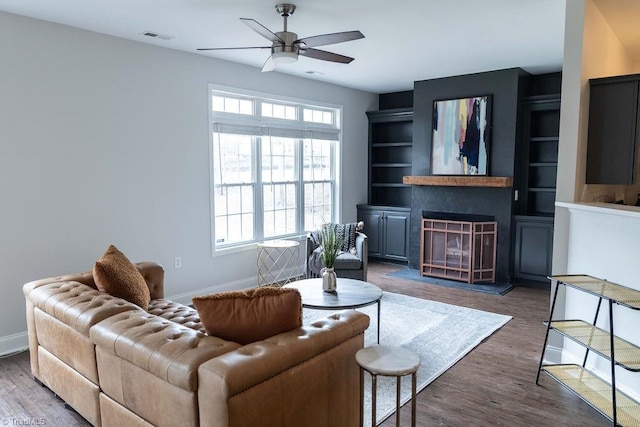 living room with ceiling fan, a large fireplace, and dark hardwood / wood-style floors