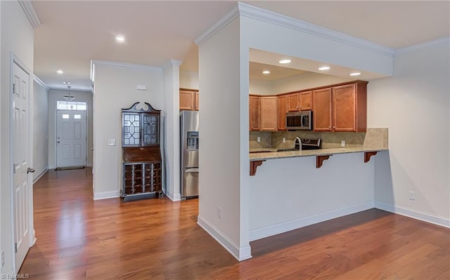 kitchen featuring stainless steel appliances, tasteful backsplash, kitchen peninsula, crown molding, and a breakfast bar