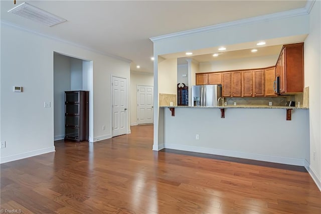 kitchen featuring stainless steel refrigerator with ice dispenser, ornamental molding, light stone counters, kitchen peninsula, and a breakfast bar area