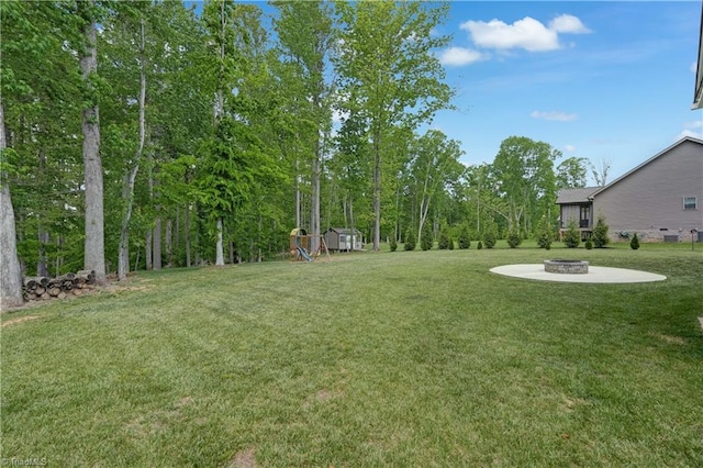 view of green lawn featuring a playground, an outdoor fire pit, a storage unit, and an outbuilding