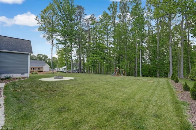 view of green lawn with a playground and a fire pit