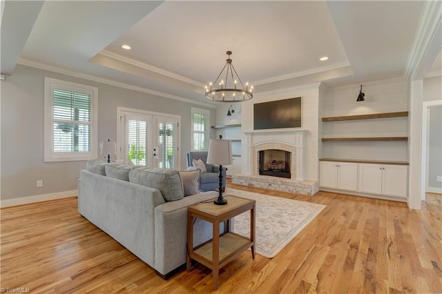 living room with a raised ceiling, french doors, light wood-style flooring, a chandelier, and ornamental molding
