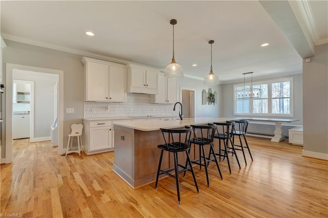 kitchen featuring ornamental molding, light countertops, white cabinetry, backsplash, and a kitchen breakfast bar
