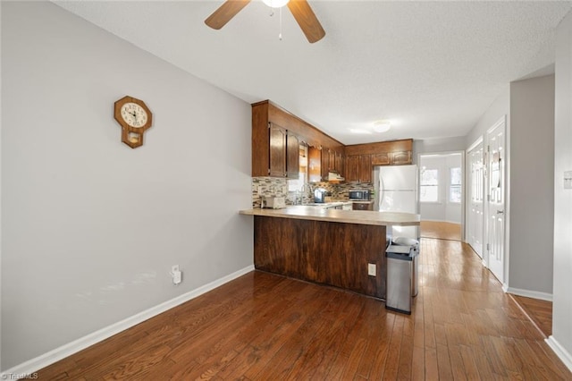 kitchen with sink, white refrigerator, dark hardwood / wood-style flooring, kitchen peninsula, and decorative backsplash