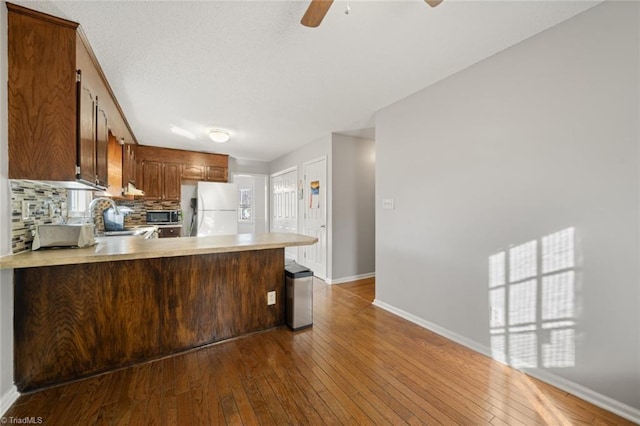 kitchen featuring sink, wood-type flooring, white refrigerator, kitchen peninsula, and backsplash