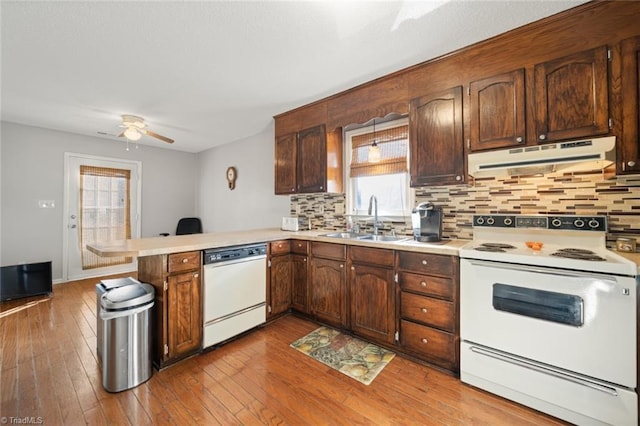 kitchen with sink, kitchen peninsula, white appliances, light hardwood / wood-style floors, and backsplash