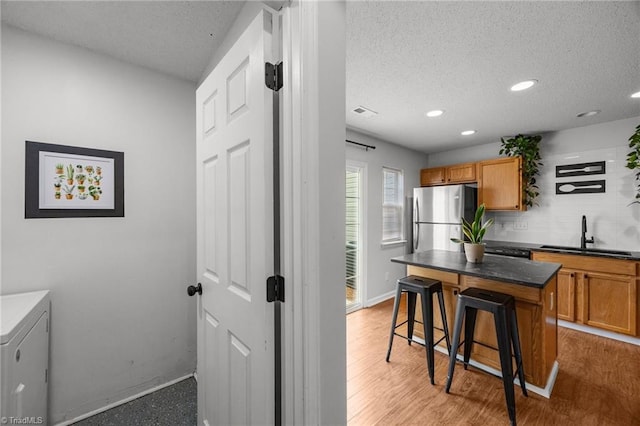 1948 Ray Alexander Dr, Greensboro, NC 27410 - kitchen with a sink, freestanding refrigerator, a breakfast bar, brown cabinets, and recessed lighting