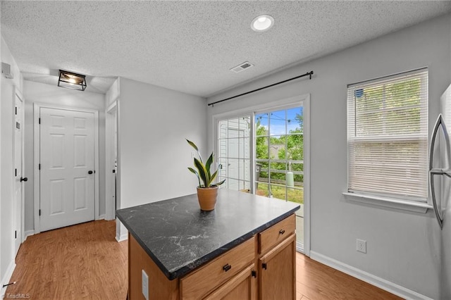 1948 Ray Alexander Dr, Greensboro, NC 27410 - kitchen with light wood-style flooring, baseboards, a textured ceiling, freestanding refrigerator, and a kitchen island