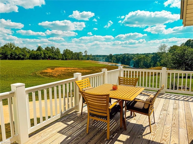 deck with outdoor dining space, a rural view, and a lawn