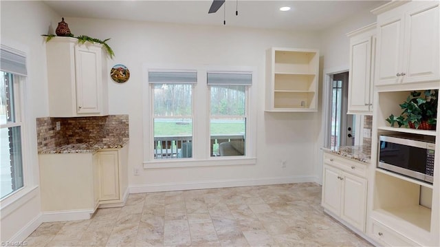 kitchen with stainless steel microwave, a ceiling fan, tasteful backsplash, open shelves, and light stone counters