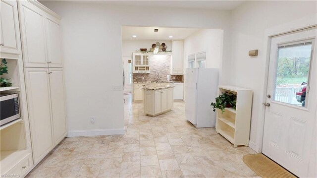 kitchen with decorative backsplash, baseboards, stainless steel microwave, pendant lighting, and freestanding refrigerator