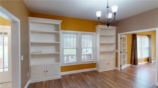 unfurnished dining area featuring built in shelves, wood finished floors, baseboard heating, baseboards, and an inviting chandelier