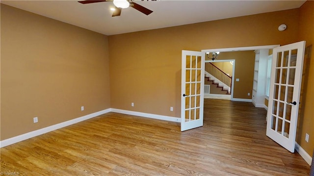 unfurnished room featuring ceiling fan with notable chandelier, wood finished floors, baseboards, and french doors