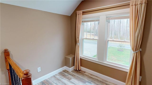 empty room featuring baseboards, lofted ceiling, and light wood-style flooring