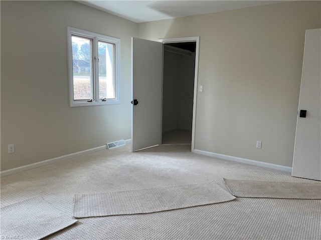 unfurnished bedroom with a walk in closet, baseboards, visible vents, and carpet flooring