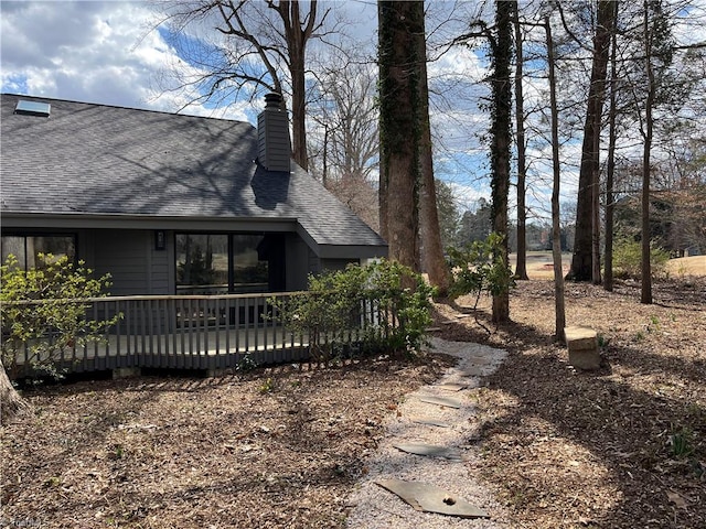 view of property exterior featuring a wooden deck, a chimney, and roof with shingles