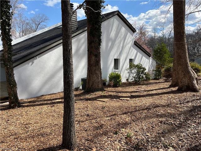 view of side of property featuring central AC, a chimney, and stucco siding