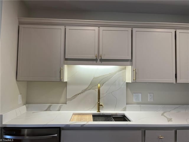 kitchen featuring light stone counters, gray cabinets, decorative backsplash, a sink, and dishwasher