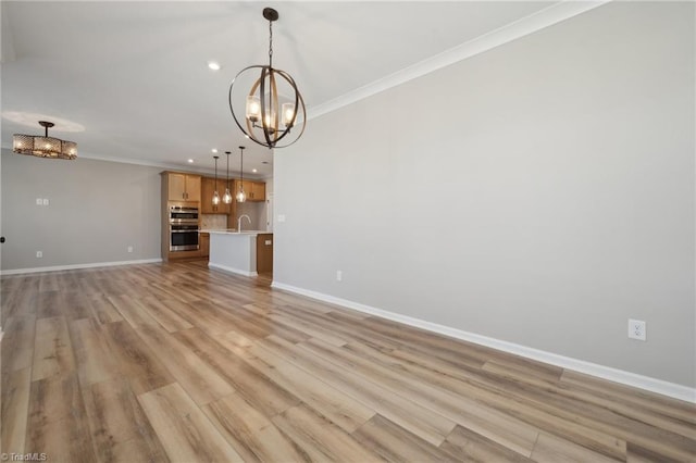 unfurnished living room with a notable chandelier, a sink, baseboards, ornamental molding, and light wood finished floors