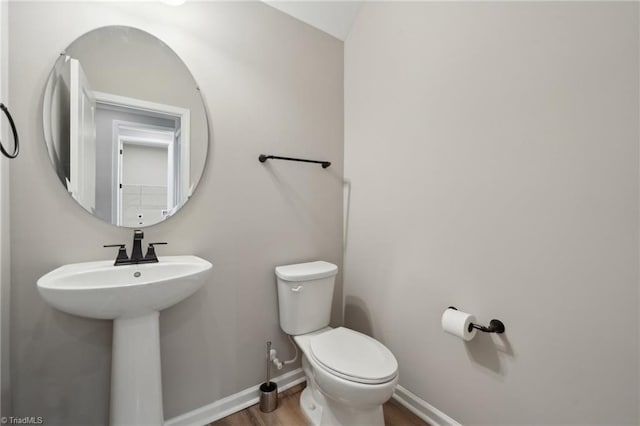 half bath featuring toilet, a sink, baseboards, and wood finished floors