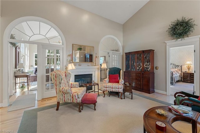 living area featuring wood finished floors, baseboards, high vaulted ceiling, french doors, and a glass covered fireplace