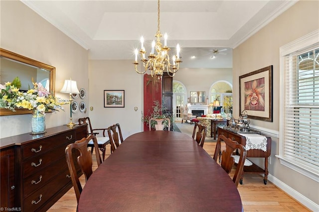 dining space featuring baseboards, a fireplace, a raised ceiling, ceiling fan with notable chandelier, and light wood-type flooring