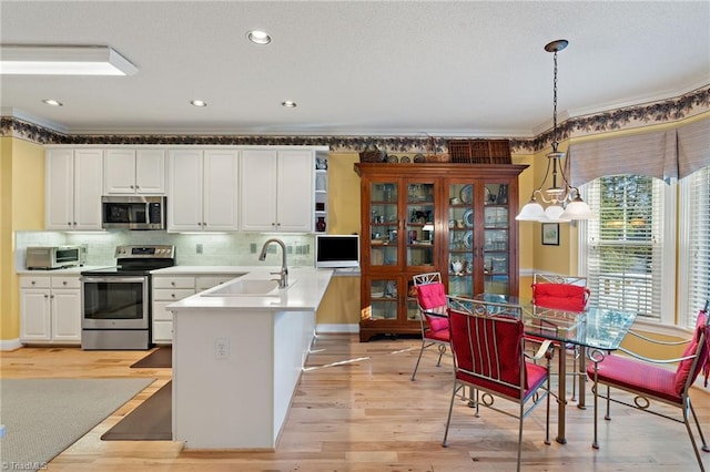 kitchen with light wood finished floors, a sink, hanging light fixtures, stainless steel appliances, and white cabinets