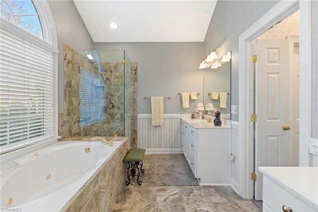 bathroom with vanity, a tub with jets, a shower stall, vaulted ceiling, and wainscoting