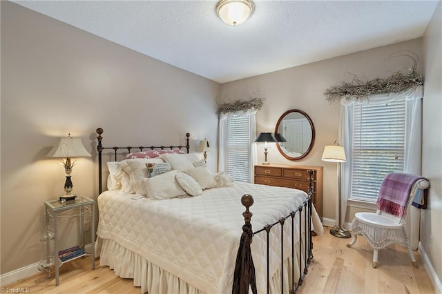 bedroom featuring a textured ceiling, baseboards, and light wood-style floors