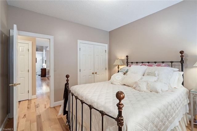 bedroom with baseboards, light wood-type flooring, a closet, and a textured ceiling