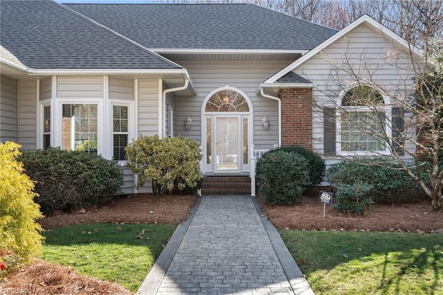 property entrance featuring brick siding and roof with shingles