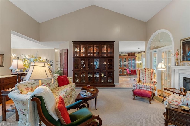 carpeted living area with a glass covered fireplace, an inviting chandelier, and high vaulted ceiling