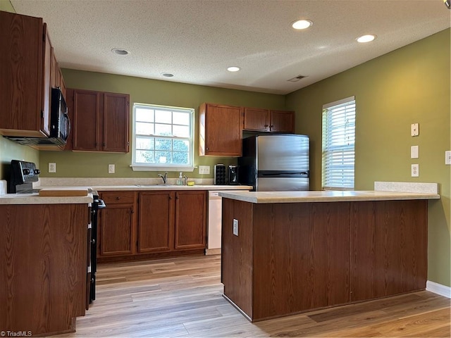 kitchen featuring light wood finished floors, a textured ceiling, appliances with stainless steel finishes, a peninsula, and light countertops