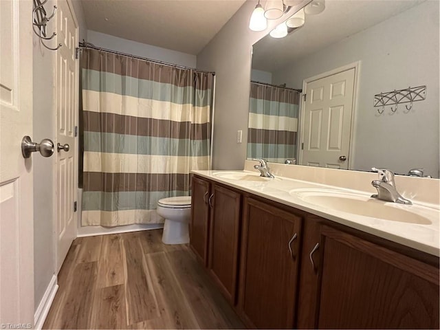 bathroom featuring double vanity, wood finished floors, a sink, and toilet