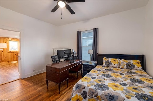 bedroom with ceiling fan, wooden walls, hardwood / wood-style floors, and multiple windows